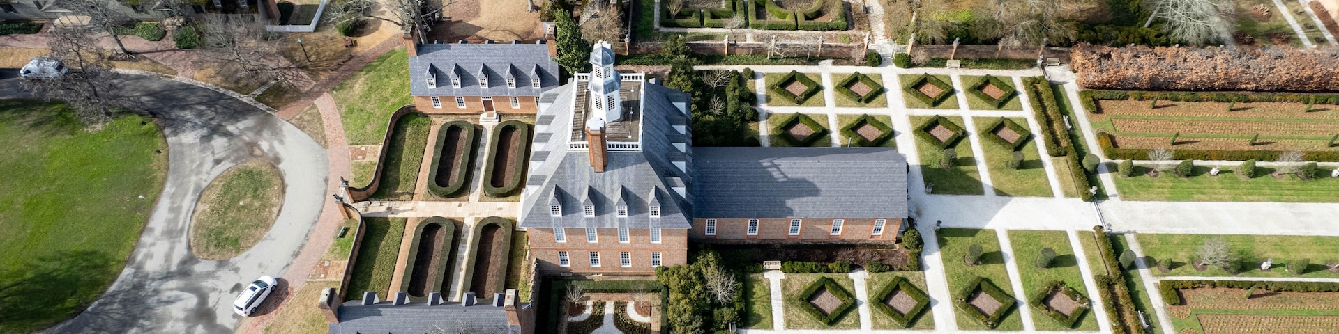 Vista aérea de uma grande propriedade com um casarão imponente, jardins formais e um caminho sinuoso.