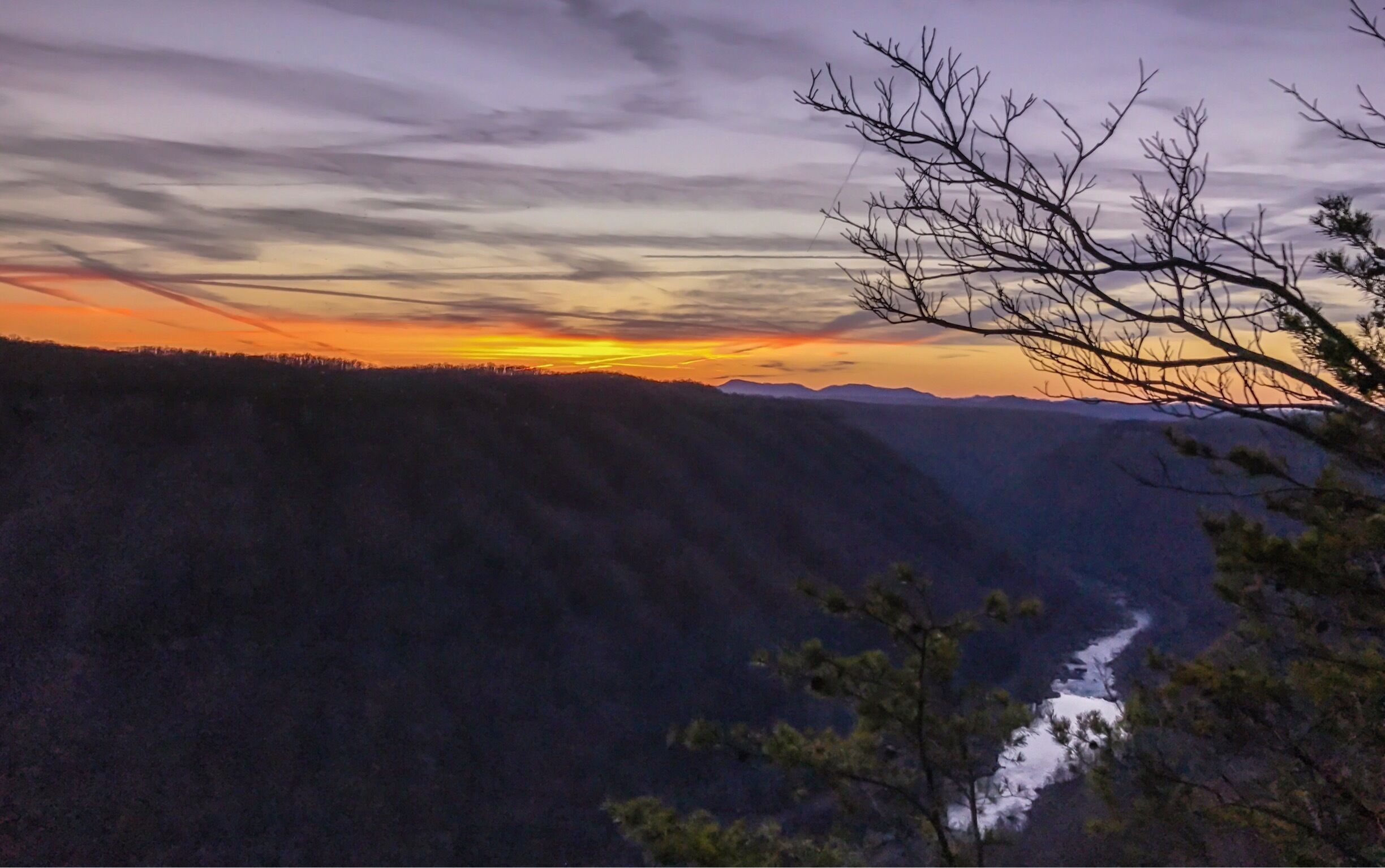 A sunset over a mountainous landscape with a river flowing through a valley.