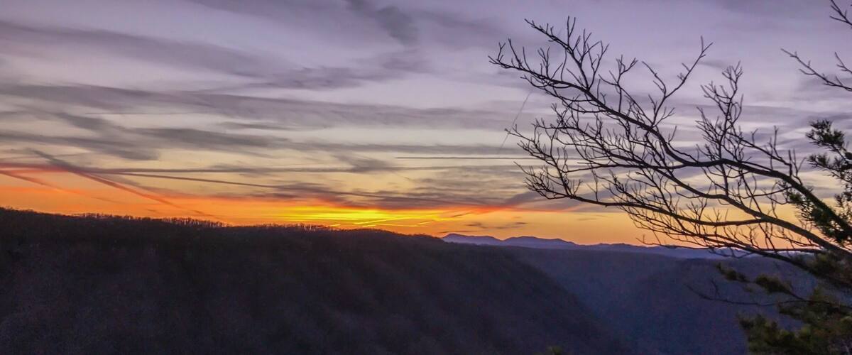 A sunset over a mountainous landscape with a river flowing through a valley.