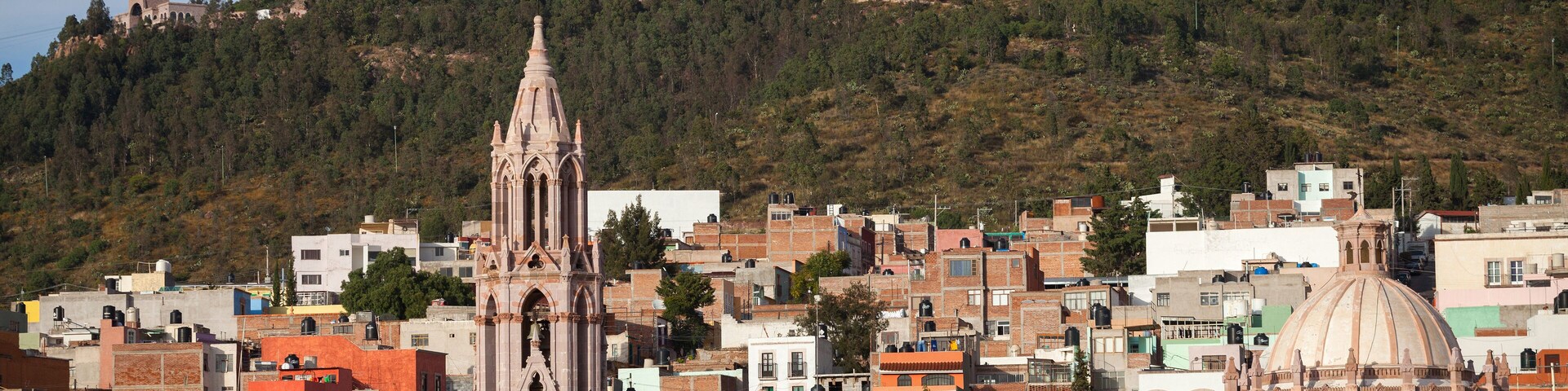 Un paisaje urbano con una catedral destacada y una colina con una iglesia en su cima.