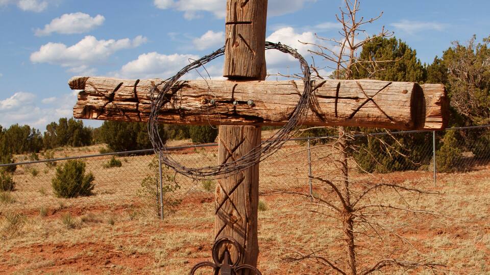 A wooden post with barbed wire and a no trespassing sign in a dry, red soil landscape.