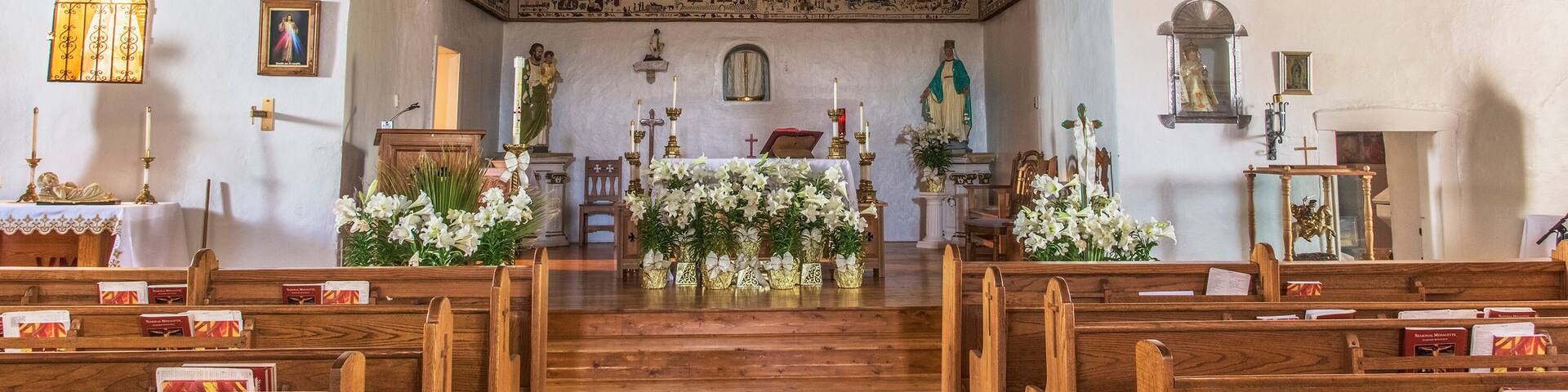 A church interior with wooden pews, a wooden altar, and religious statues.