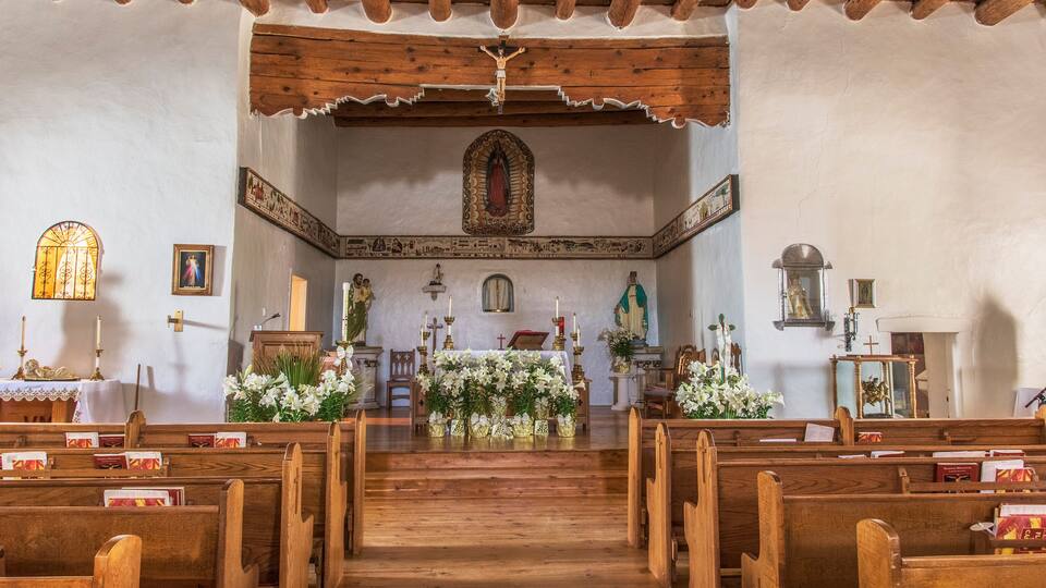 A church interior with wooden pews, a wooden altar, and religious statues.