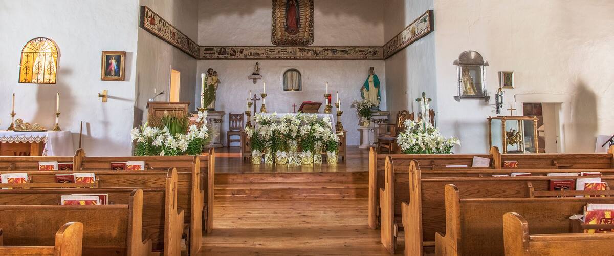 A church interior with wooden pews, a wooden altar, and religious statues.