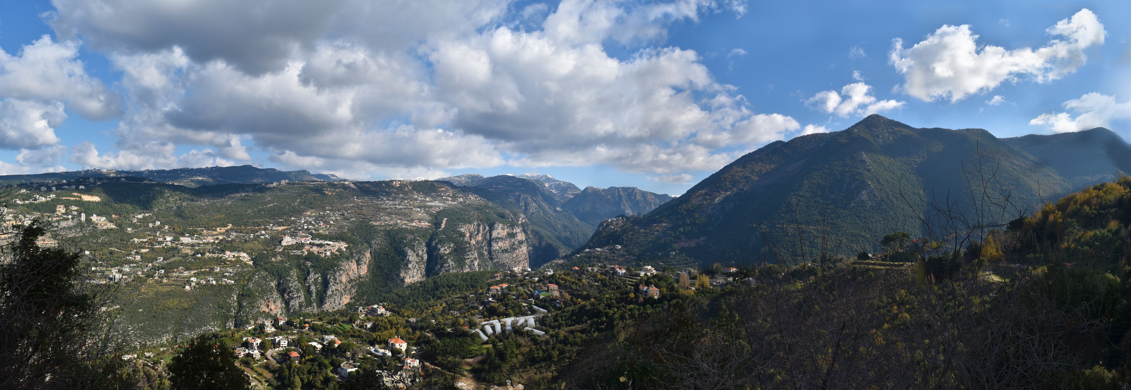 A mountainous landscape with a village nestled in the valley, surrounded by steep cliffs and dense forests.