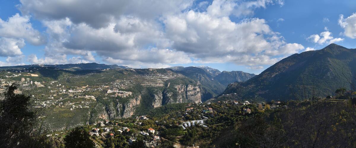 A mountainous landscape with a village nestled in the valley, surrounded by steep cliffs and dense forests.