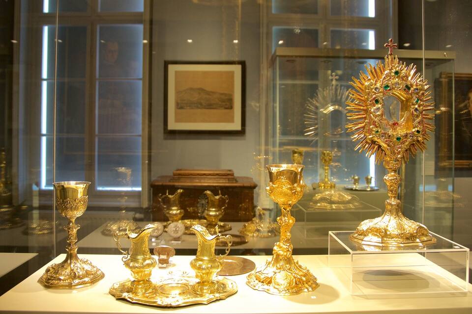 Presentatie van sierlijke gouden artefacten, waaronder een groot object in de vorm van een boom met een kruis bovenop, in een museum.