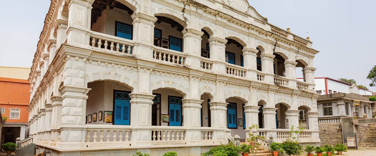 A historic building with white walls, blue doors, and multiple arches.