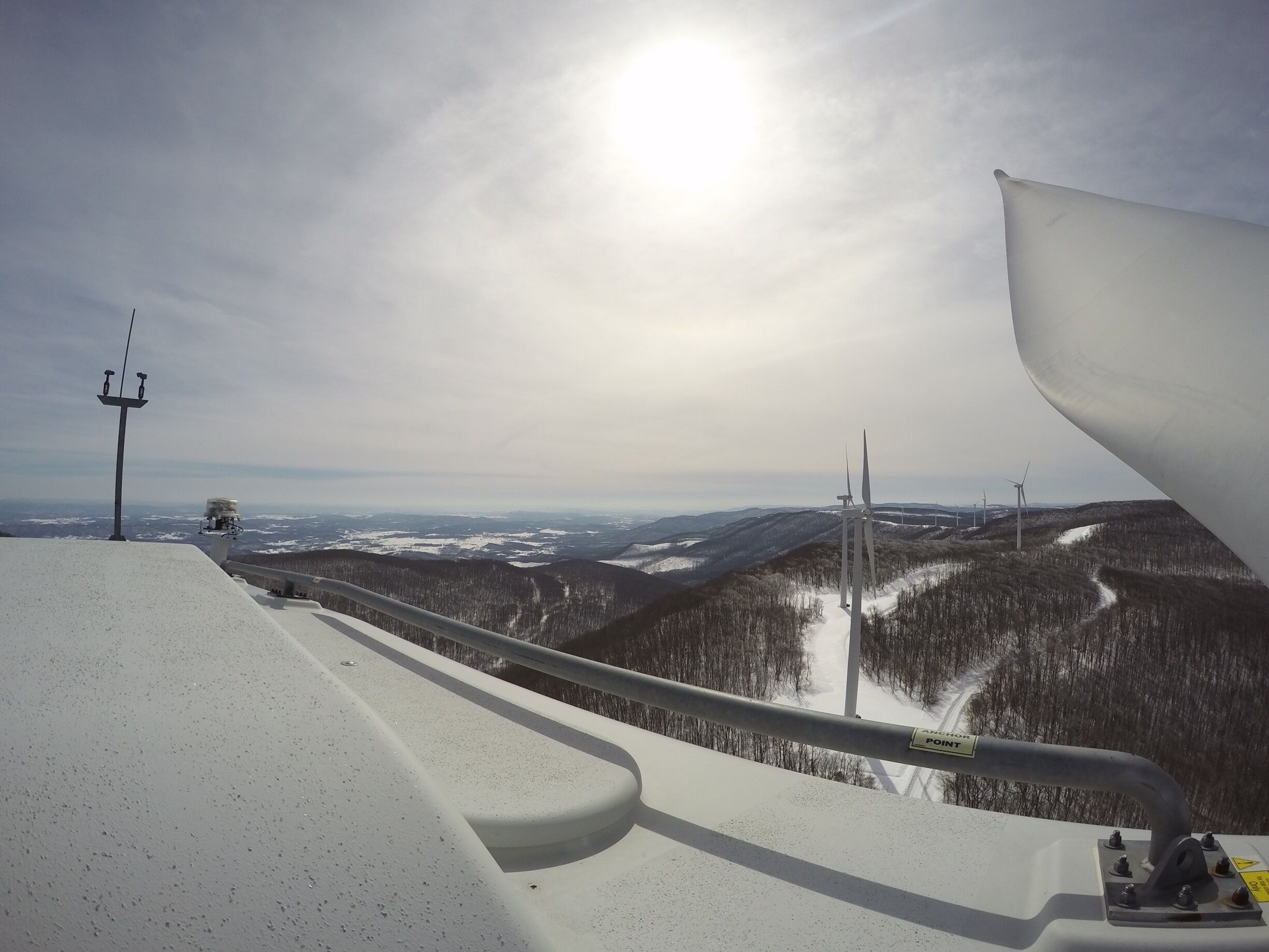 A snowy mountain landscape with a ski lift and wind turbines in the distance.