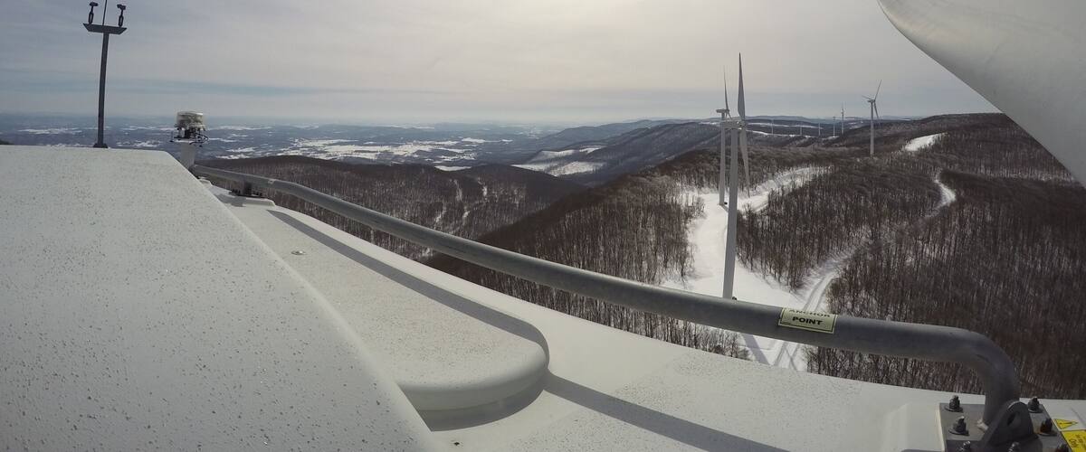 A snowy mountain landscape with a ski lift and wind turbines in the distance.