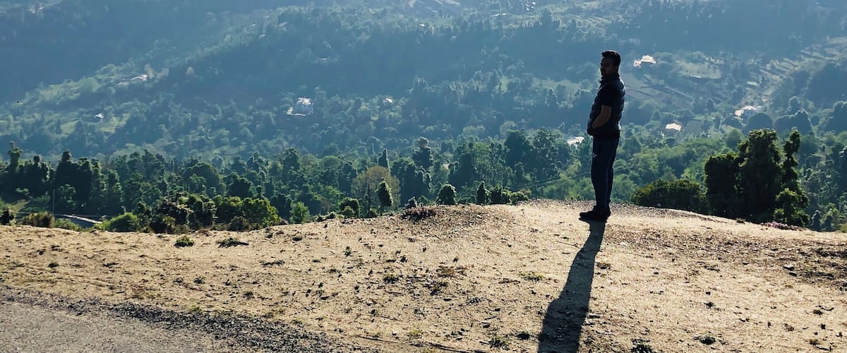 A person standing on a hill overlooking a valley with scattered buildings and dense forest.