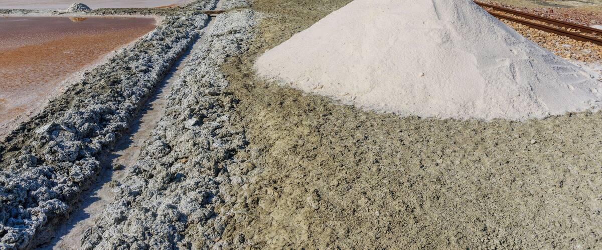 A salt flat with large white salt piles and a railway track.