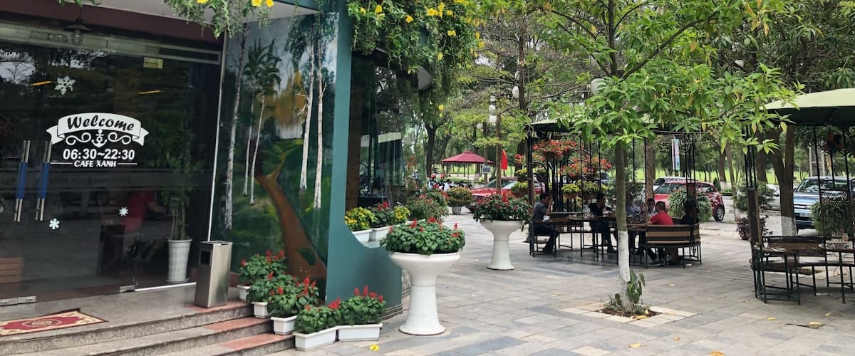 A cafe with outdoor seating, surrounded by greenery and potted plants.