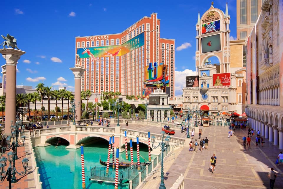 A bustling casino area with a large building featuring a prominent 'Treasure Island' sign, a fountain, and a pool with gondolas.