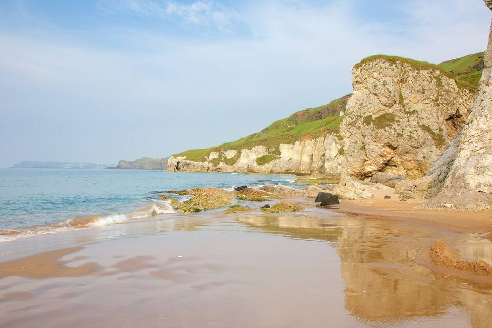 A coastal landscape with a sandy beach, rocky cliffs, and calm sea.
