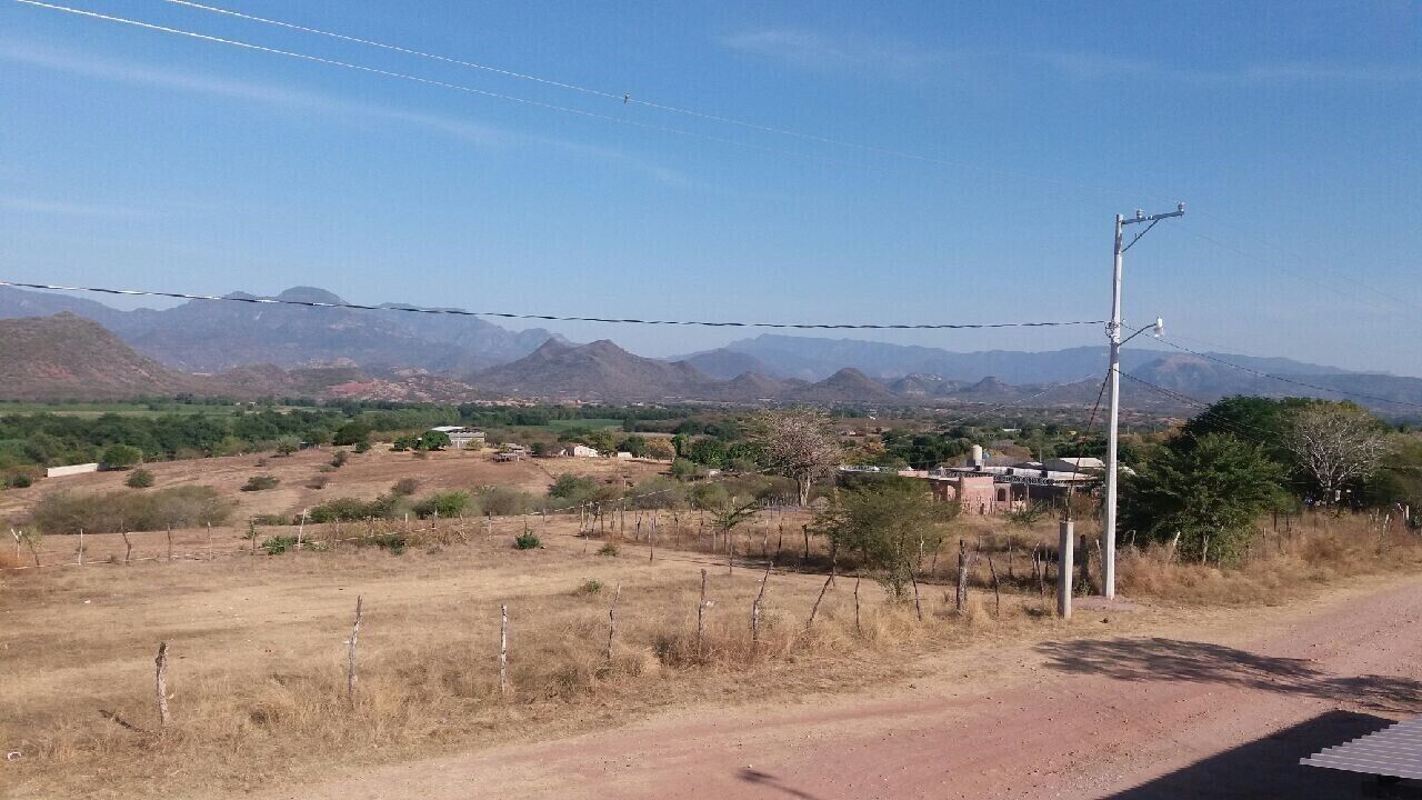 A rural landscape with mountains in the background, a dirt road, and sparse vegetation.