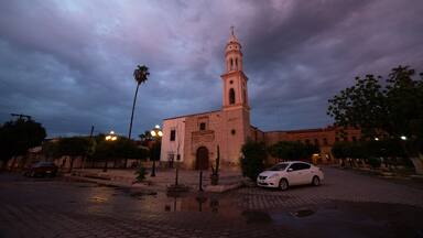 A historic church with a bell tower, surrounded by palm trees and a cobblestone street.