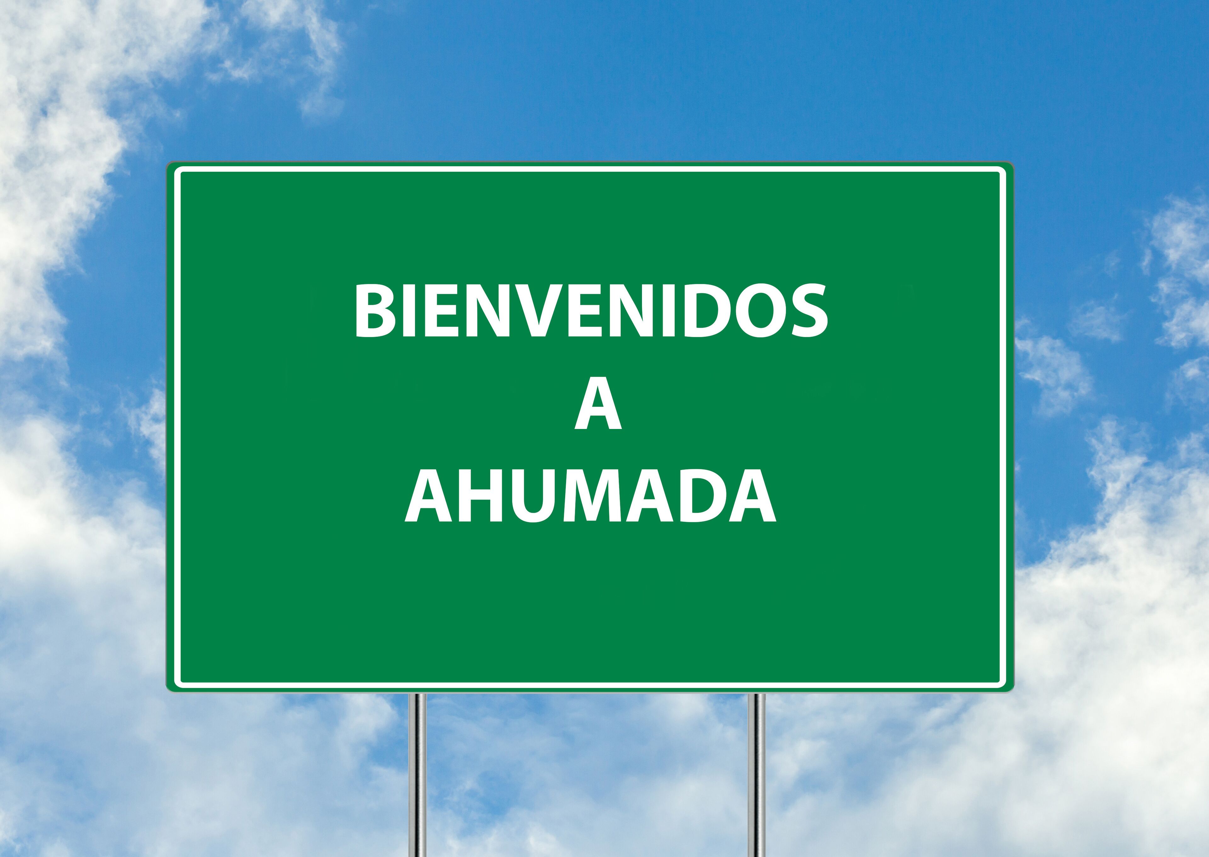 A green welcome sign with the text "BIENVENIDOS A AHUMADA" against a blue sky with clouds.