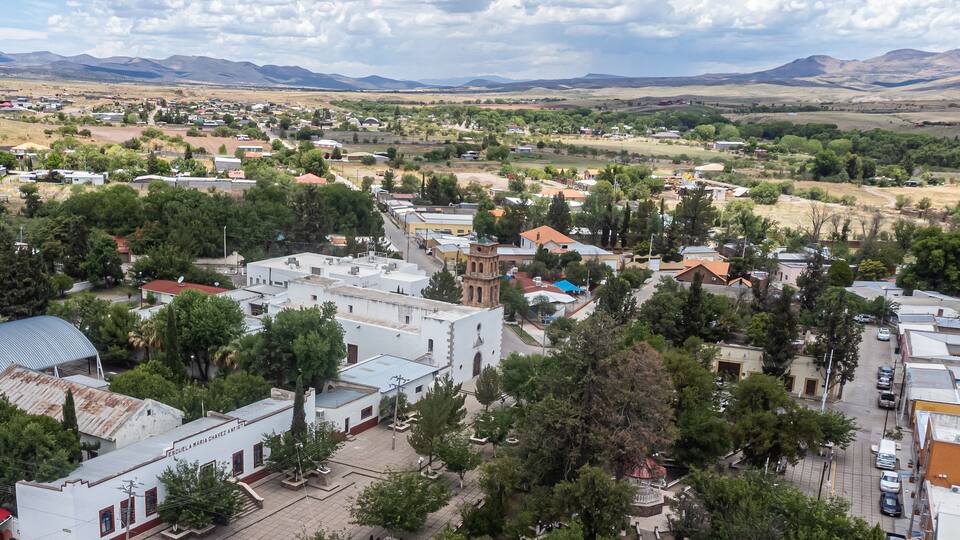 A town with a prominent church, surrounded by greenery and mountains in the background.