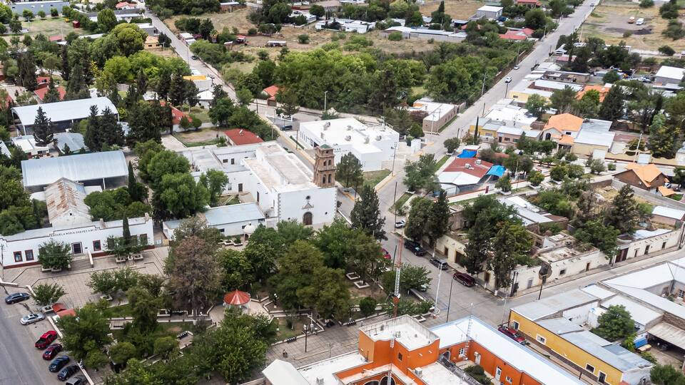 An aerial view of a town with a mix of residential and commercial buildings, a prominent church, and a central plaza with a gazebo.