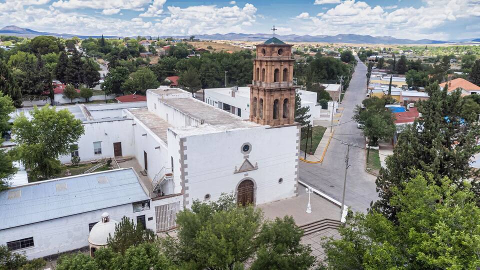 A church with a bell tower, surrounded by trees and buildings.