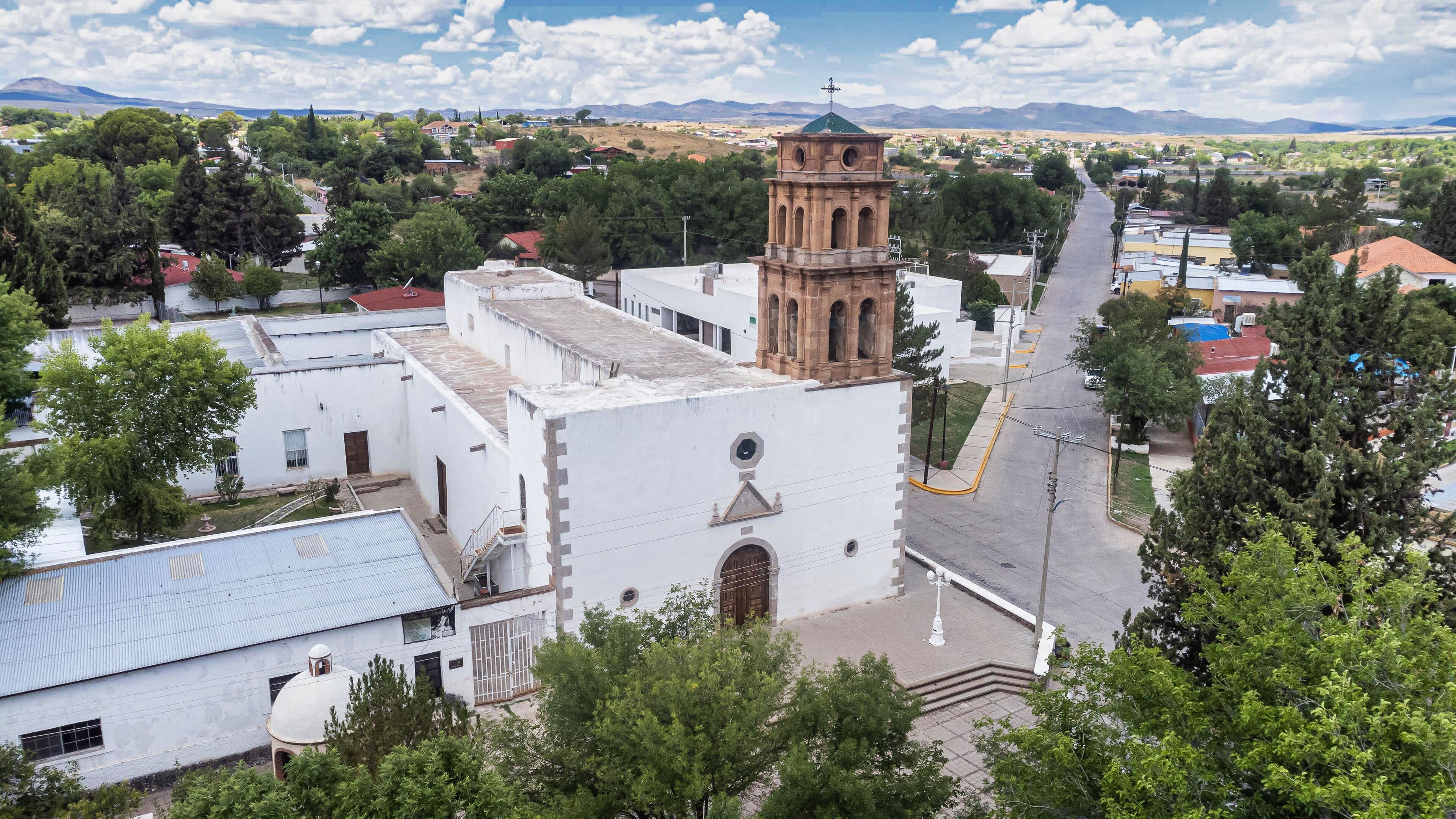 A church with a bell tower, surrounded by trees and buildings.