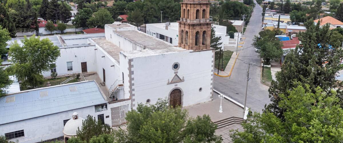 A church with a bell tower, surrounded by trees and buildings.