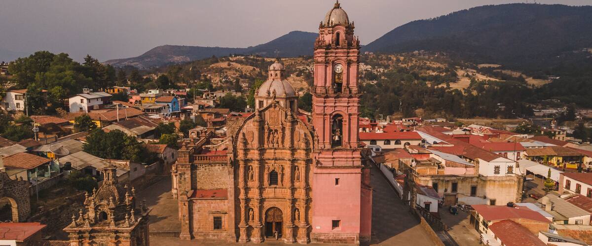 A historic church with a bell tower and a dome, surrounded by a town with red-roofed buildings.