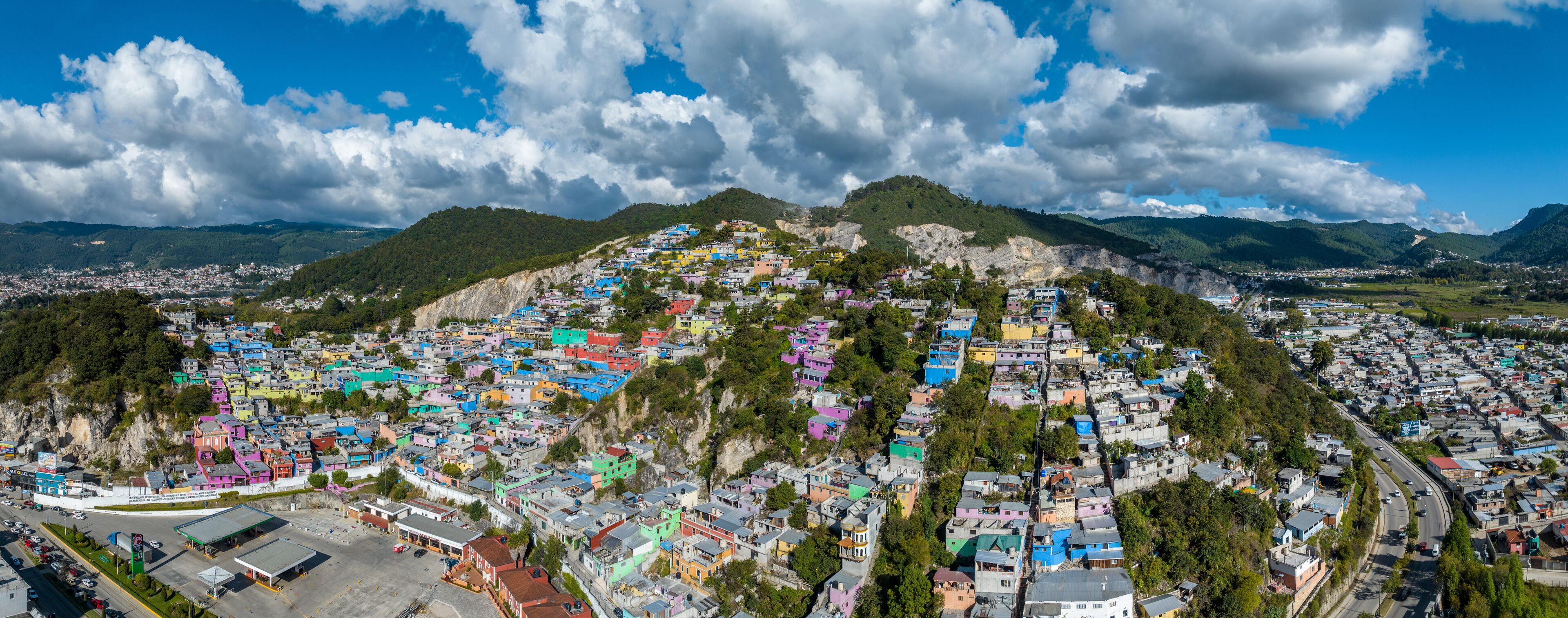 A colorful hillside town with a mix of residential buildings and a gas station.