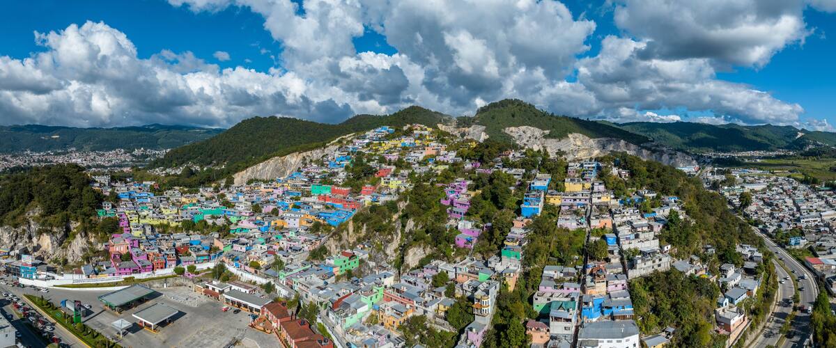 A colorful hillside town with a mix of residential buildings and a gas station.