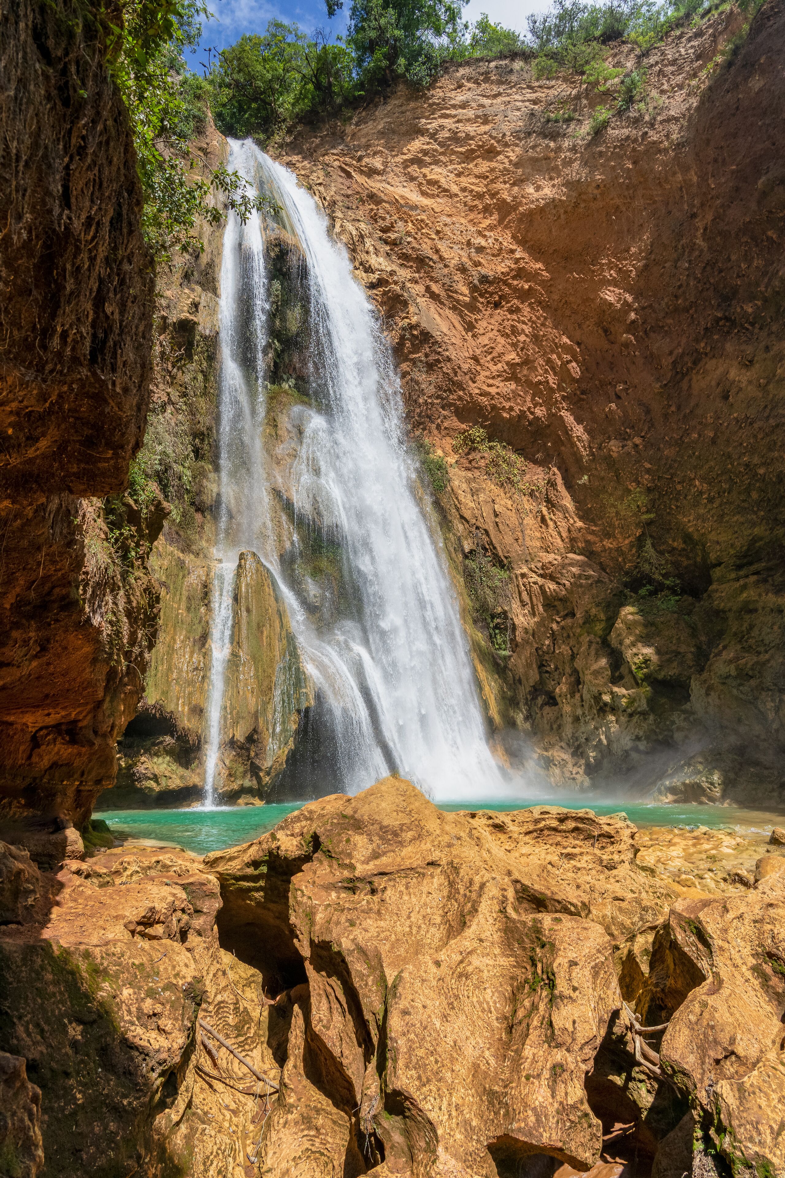 A waterfall cascading into a turquoise pool surrounded by rocky terrain and greenery.