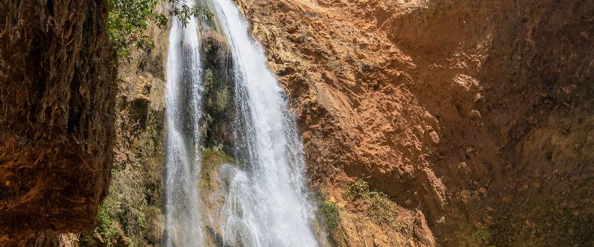 A waterfall cascading into a turquoise pool surrounded by rocky terrain and greenery.