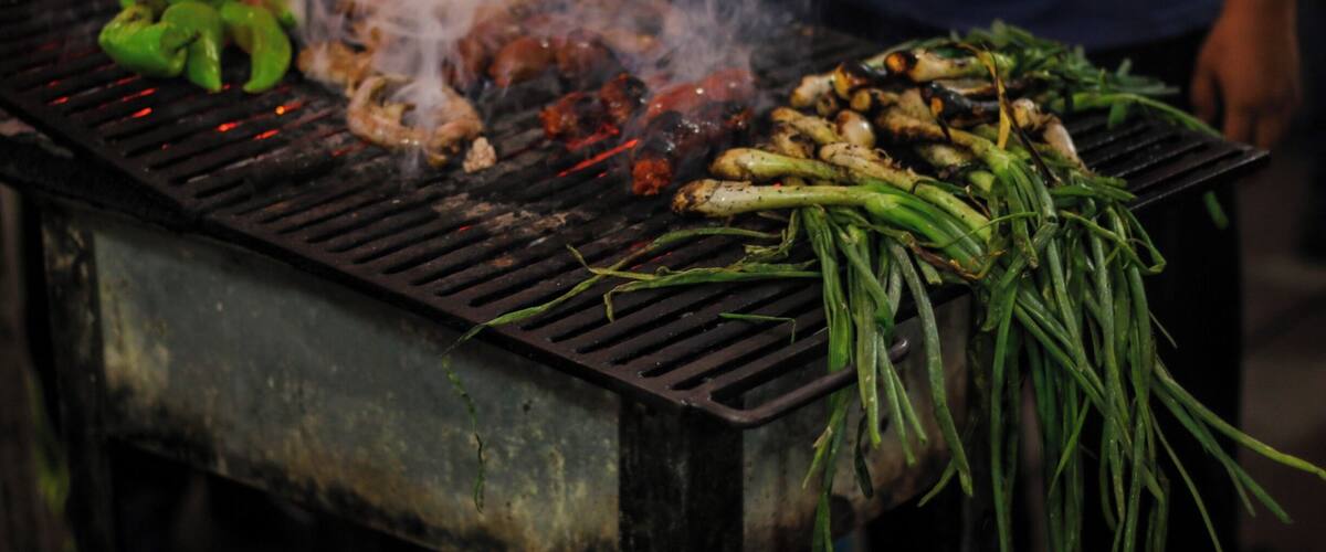 A grill with various meats and vegetables being cooked over an open flame.