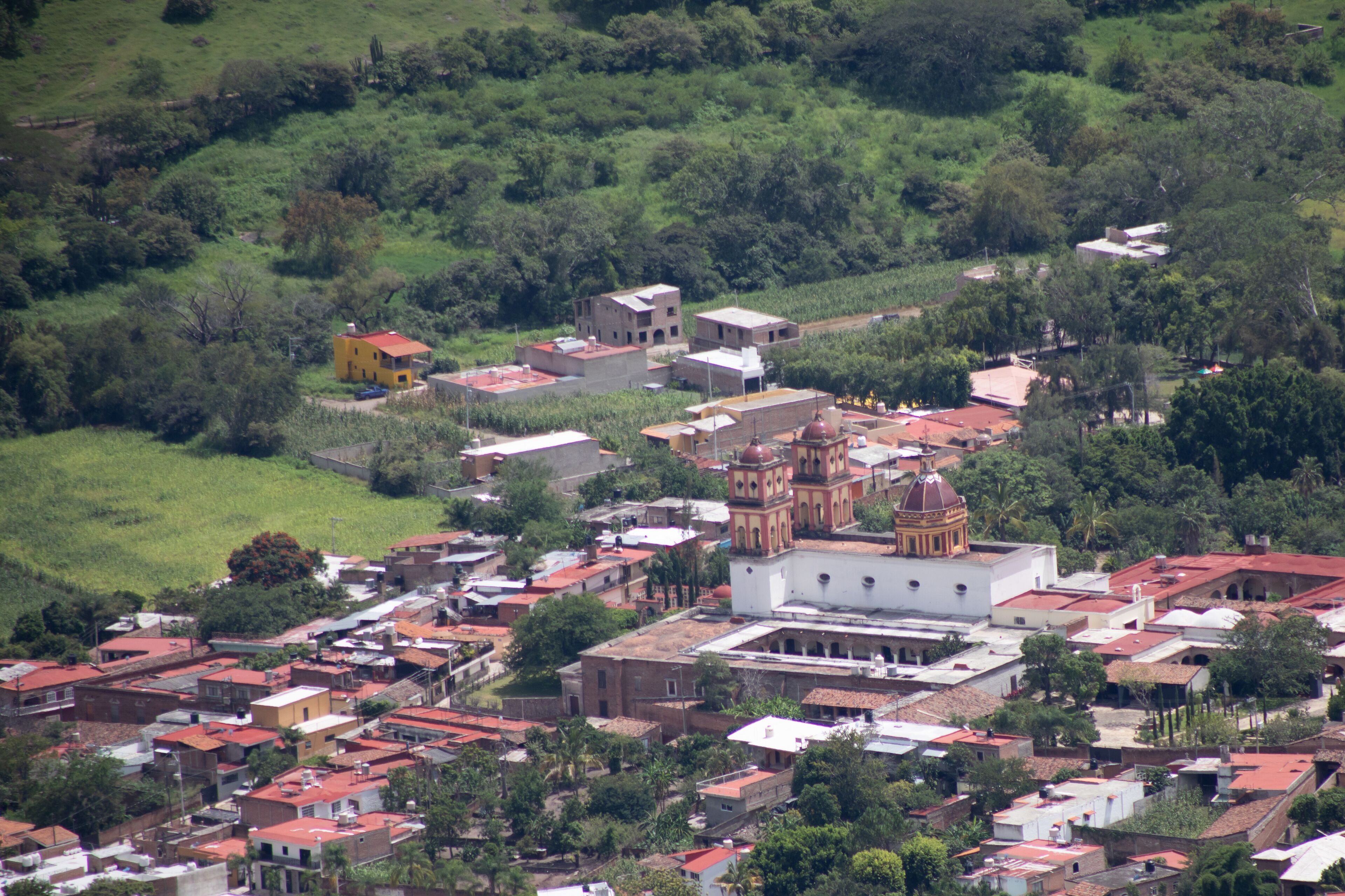 A town with a prominent church featuring a dome and bell tower, surrounded by residential buildings and lush greenery.