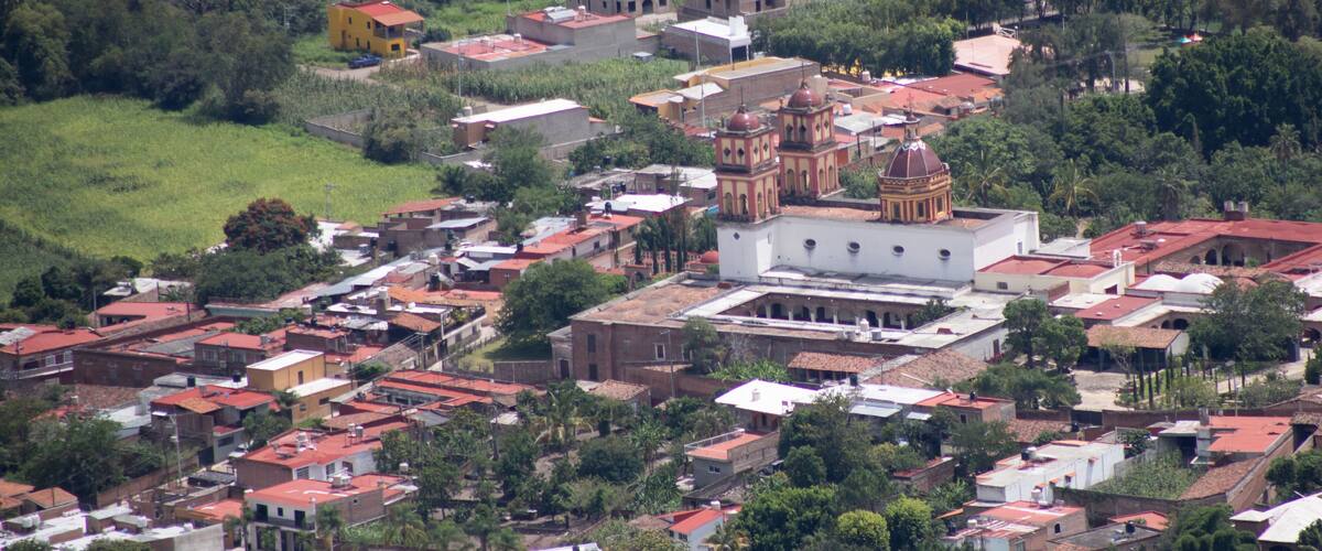 A town with a prominent church featuring a dome and bell tower, surrounded by residential buildings and lush greenery.