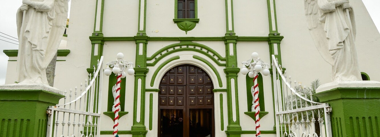Una iglesia con fachada verde y blanca, un campanario y estatuas de ángeles.