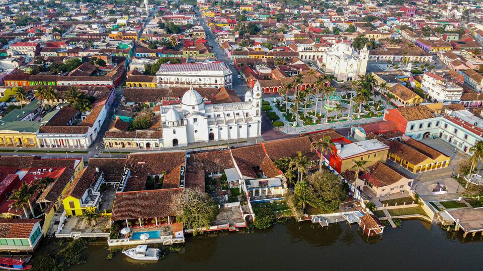 A coastal city with colorful buildings, a prominent white church, and a marina with boats.