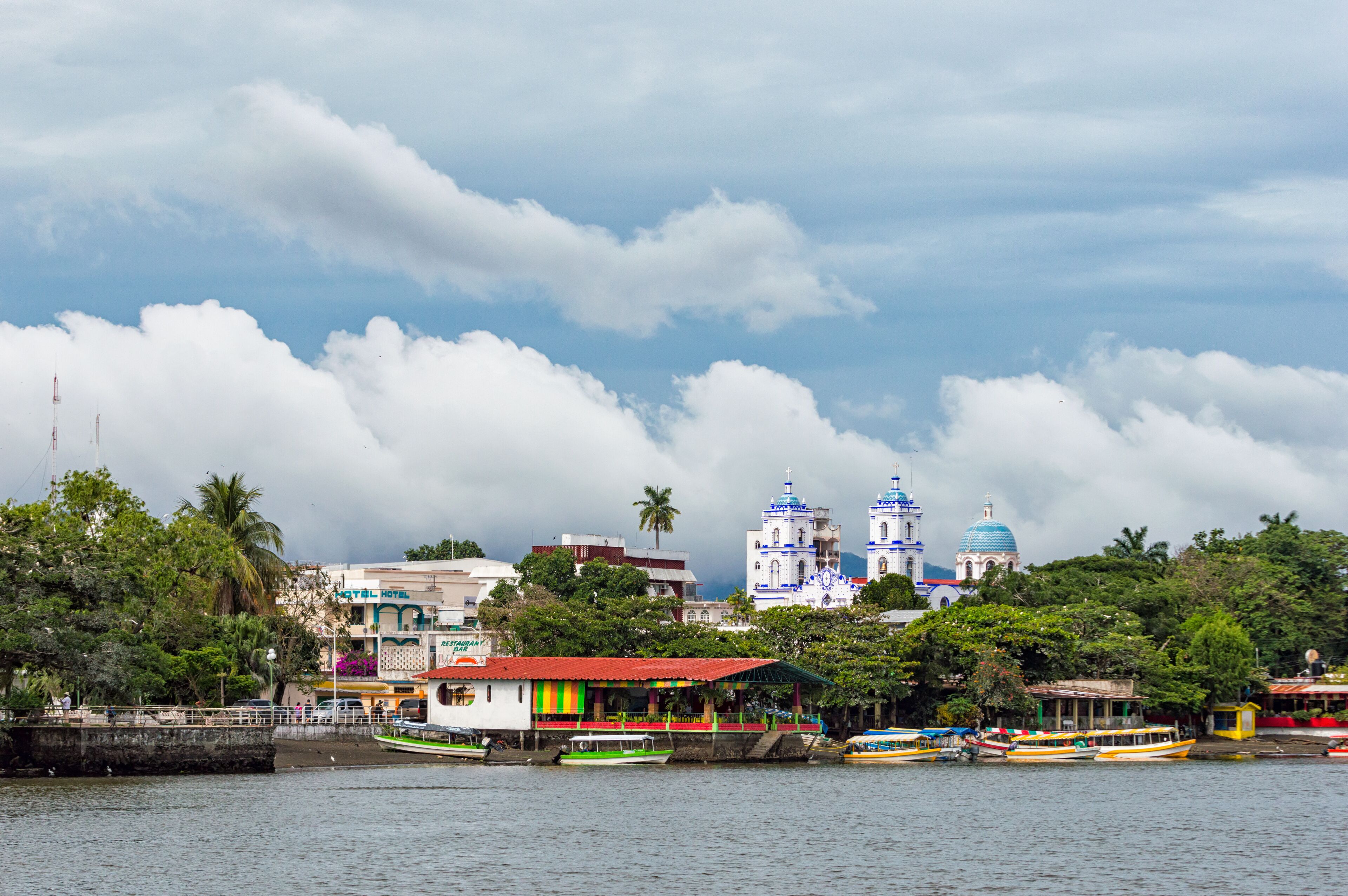A waterfront with colorful buildings, a church with blue domes, and boats on the water.