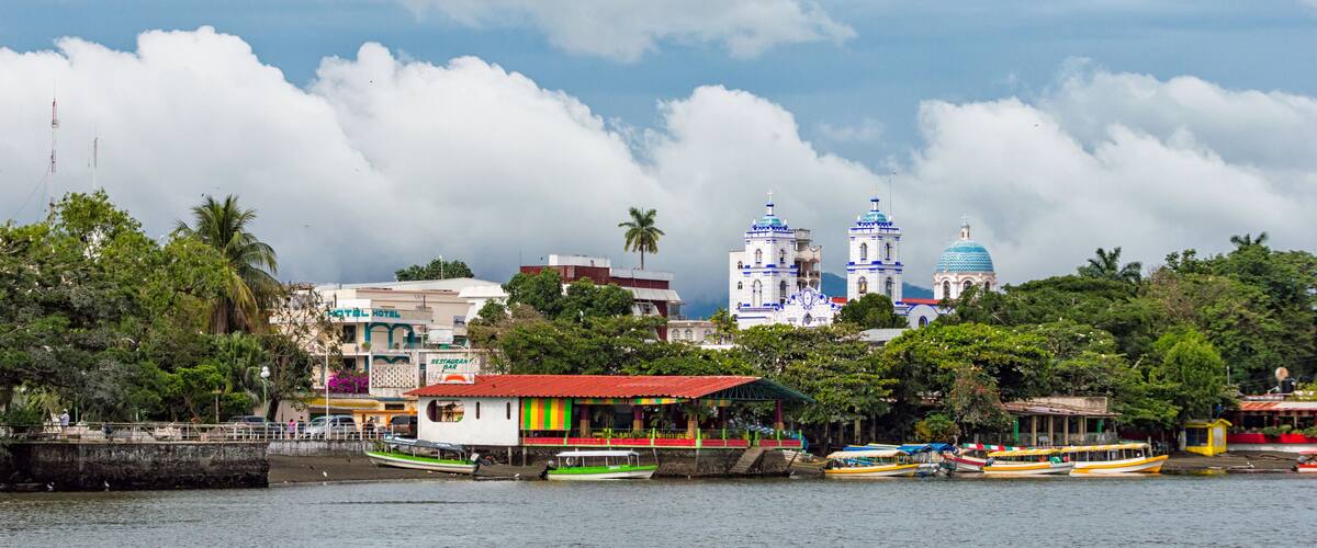 A waterfront with colorful buildings, a church with blue domes, and boats on the water.