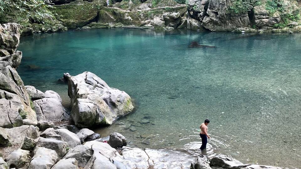 A clear turquoise river surrounded by large rocks and lush greenery.
