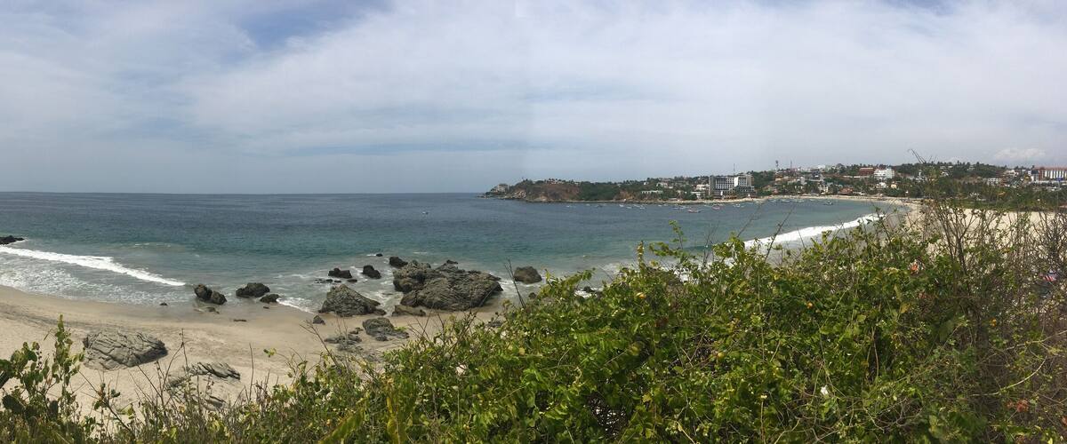 A coastal landscape with a sandy beach, rocky outcrops, and a town in the distance.