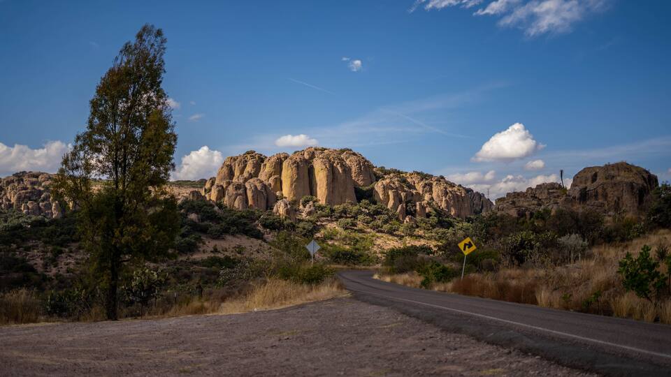A winding road leading to a rocky mountain range with a clear sky.