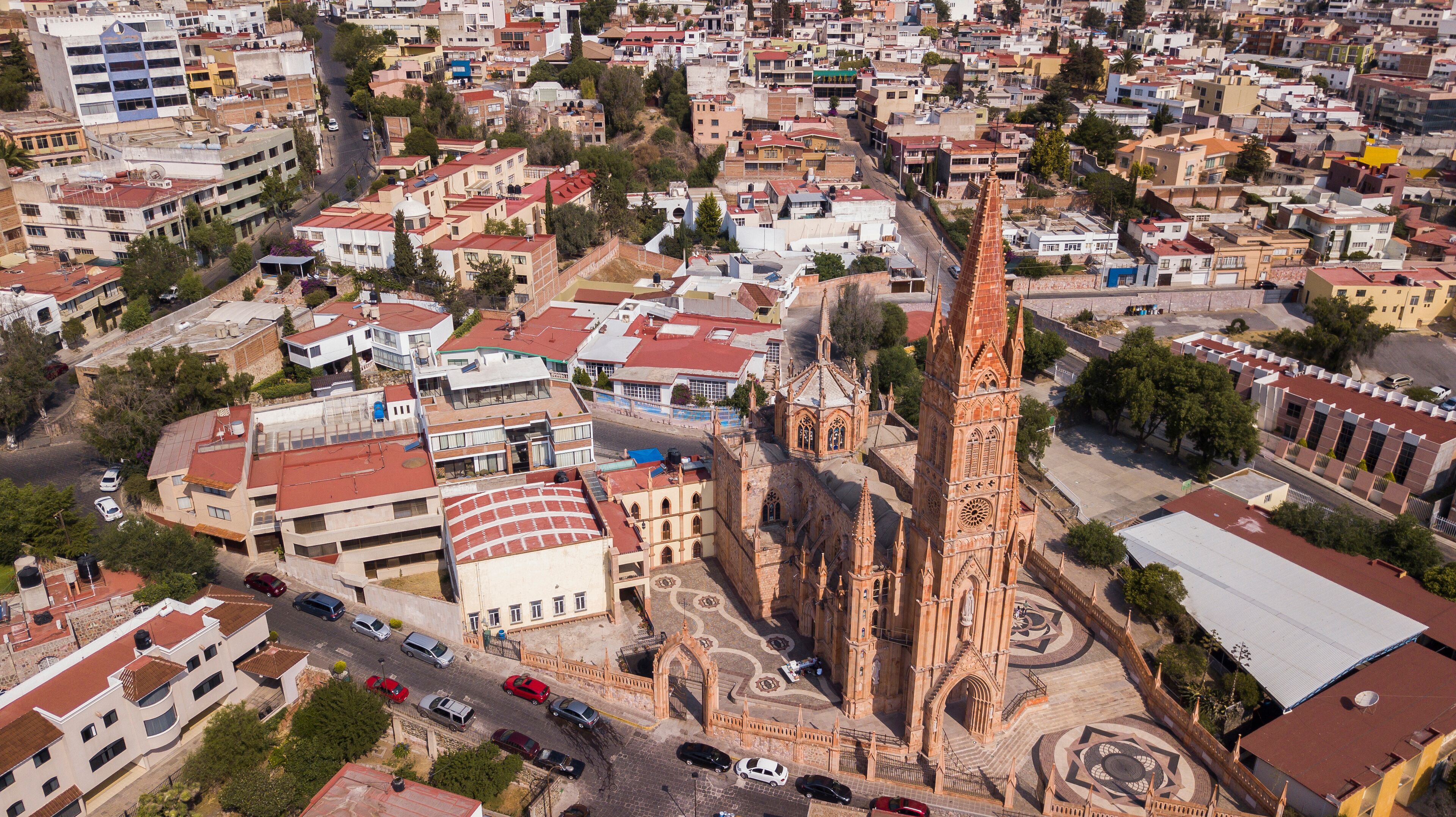An aerial view of a city with a prominent church featuring a tall spire and intricate architecture.