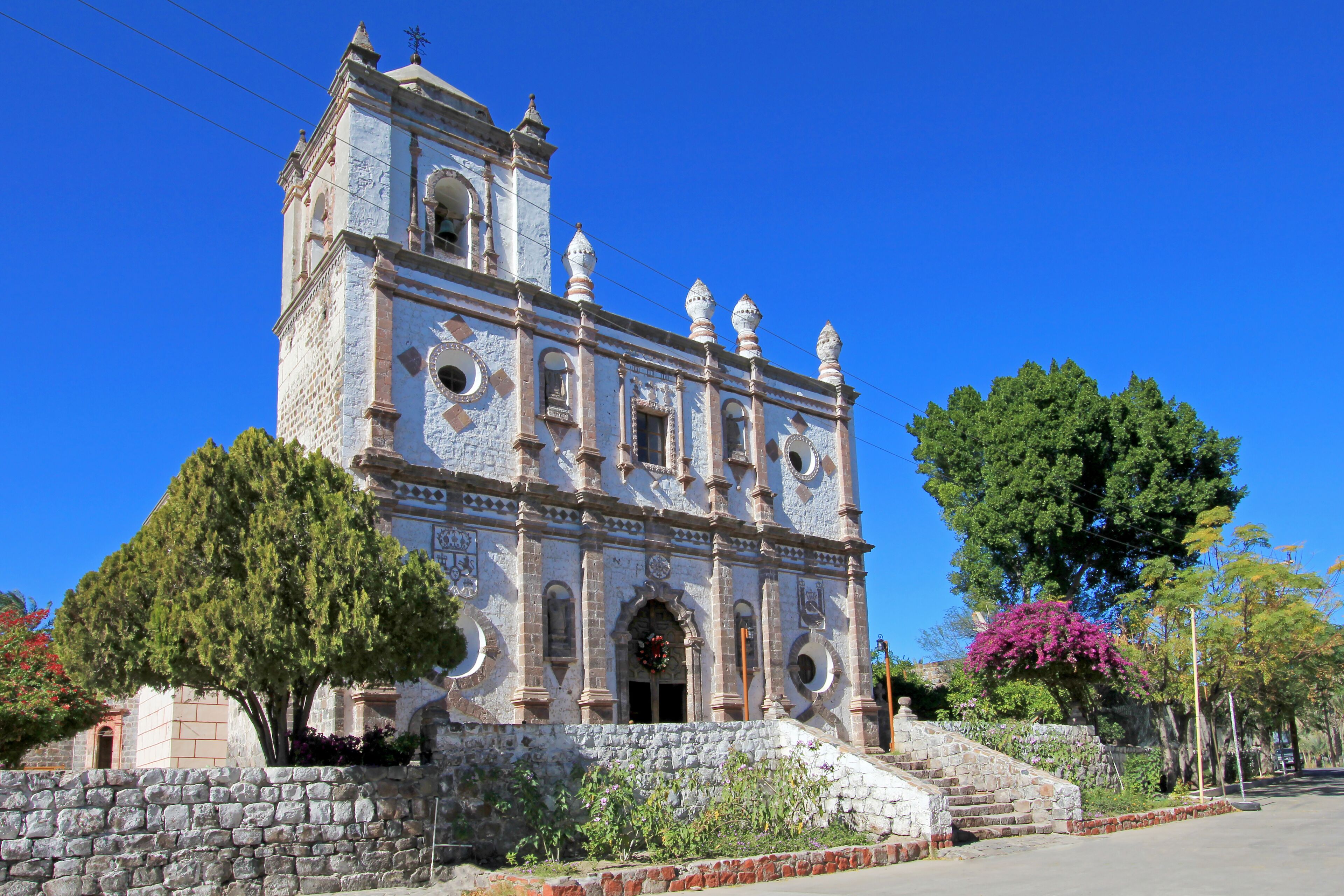A historic church with a bell tower, surrounded by trees and a stone wall.