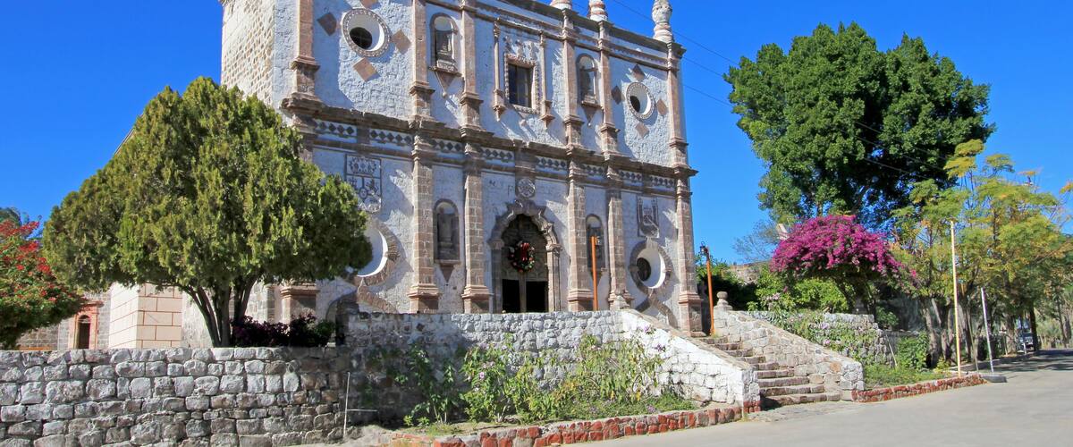 A historic church with a bell tower, surrounded by trees and a stone wall.