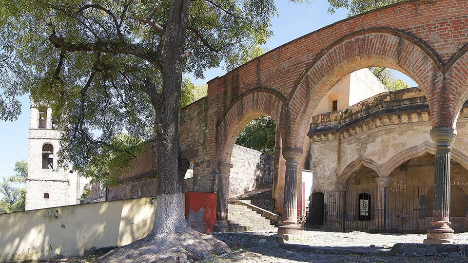 An ancient brick archway with columns, surrounded by trees and a stone wall.