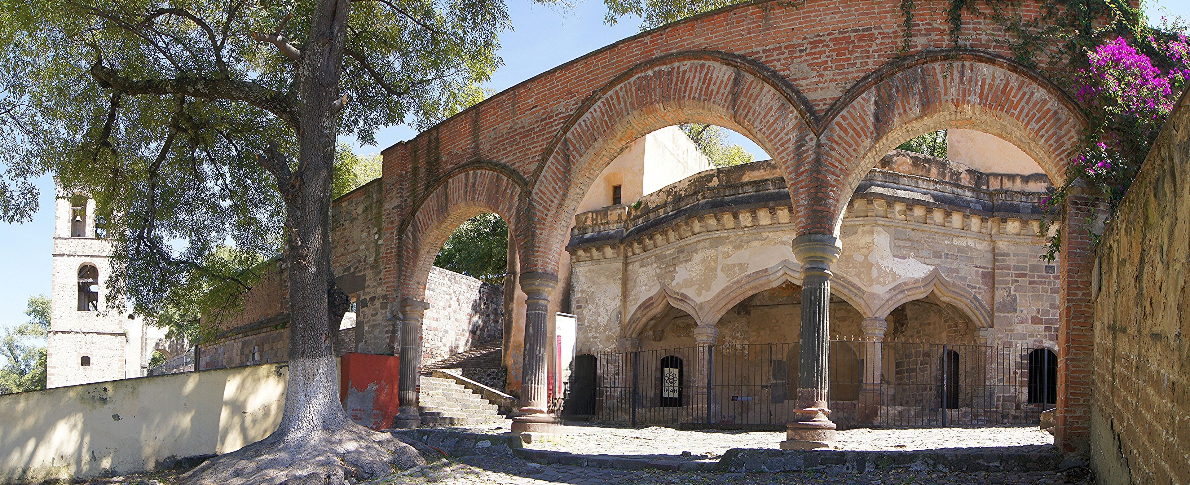 An ancient brick archway with columns, surrounded by trees and a stone wall.