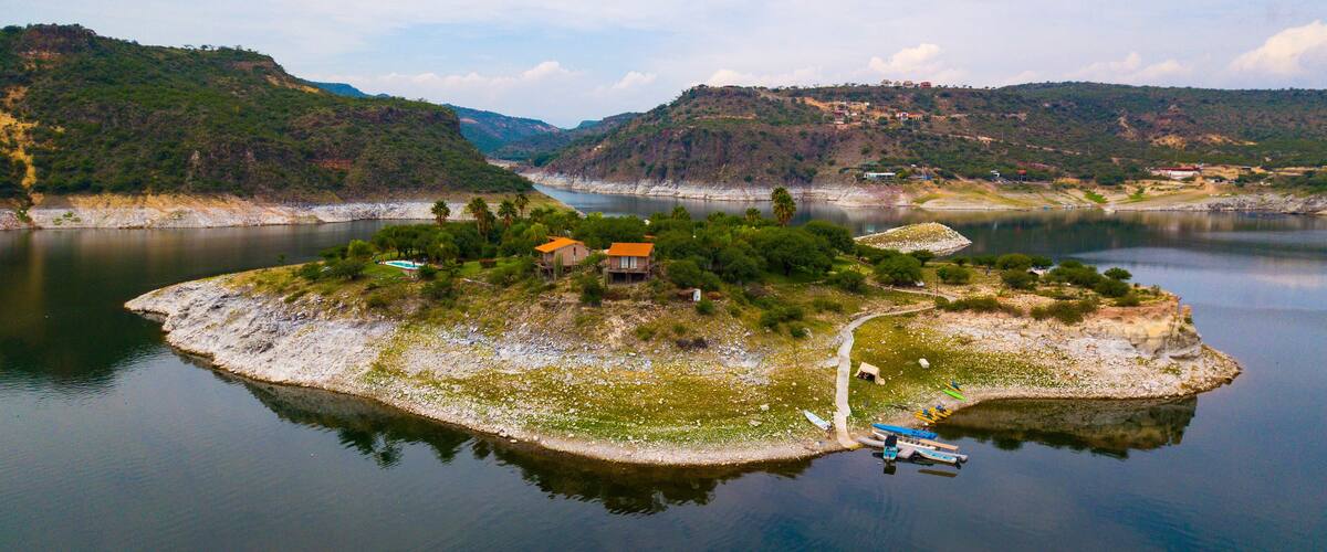 A small island with houses and a dock in a calm lake surrounded by hills.