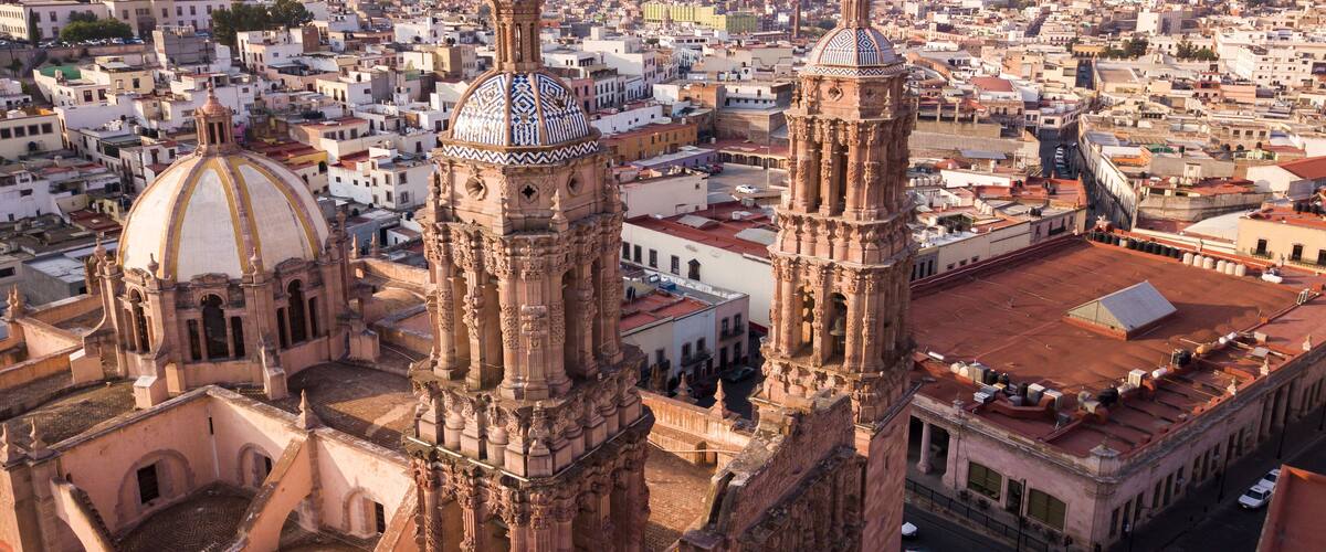 A cathedral with two prominent towers and a large dome, surrounded by a densely packed cityscape with mountains in the background.