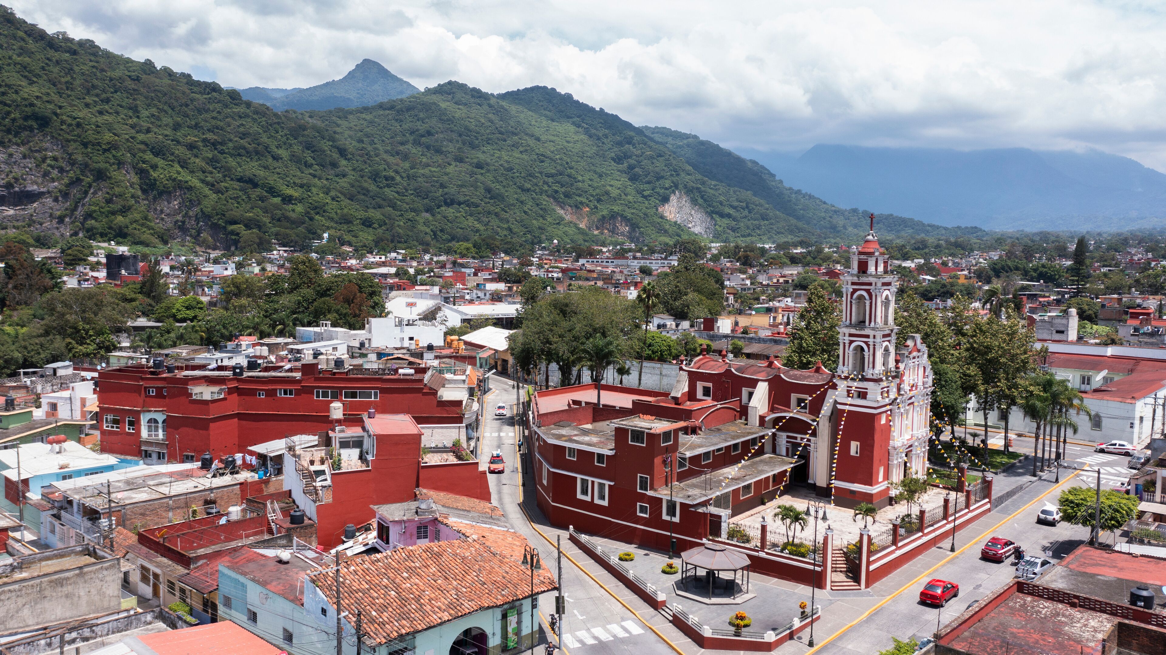 A town with a prominent church, red-roofed buildings, and a mountainous backdrop.